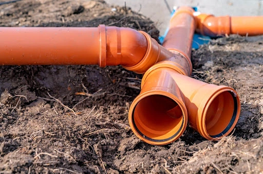 Close-up of orange PVC sewer pipes laid out on rough ground, connected at various joints for a drainage system installation.